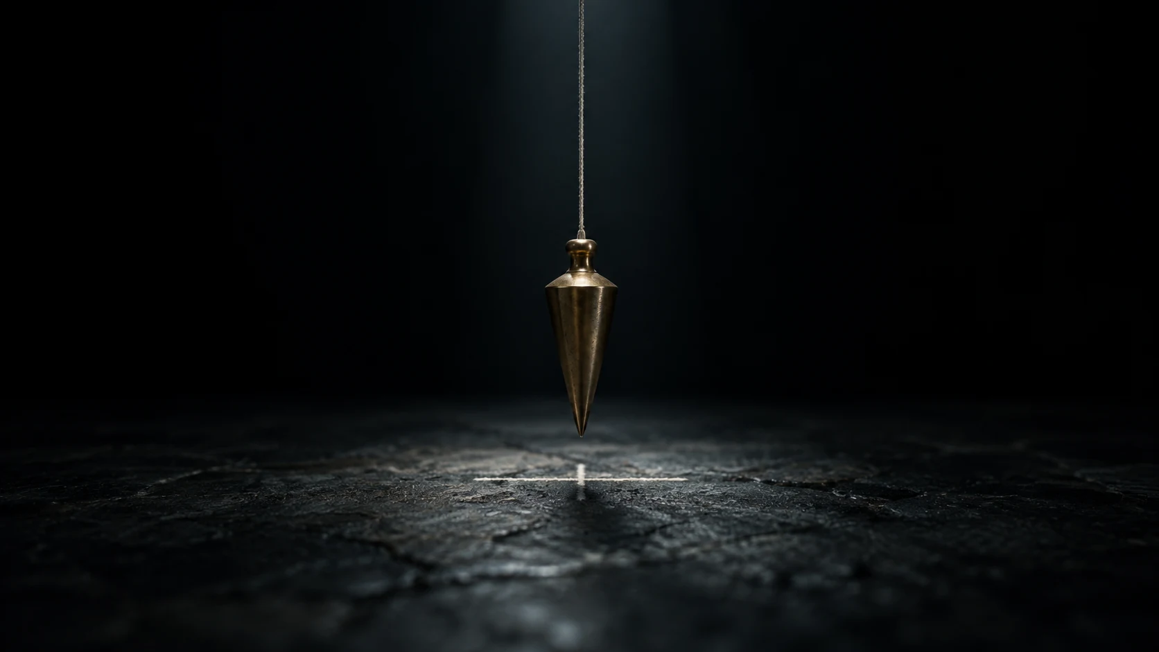 An editorial photograph of a brass plumb bob hanging dead still on a thin cord in a dark, empty space, lit by a single narrow beam from above. Its point hovers just over a faint chalk cross on a cracked dark stone floor.