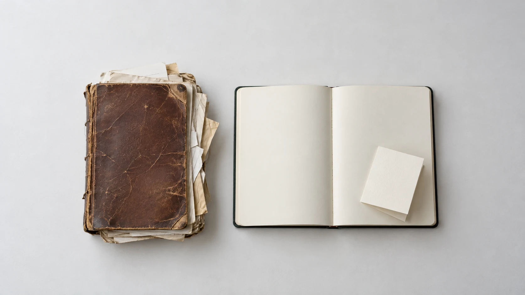 An editorial photograph of two notebooks seen from directly above on a pale grey surface. On the left lies a worn brown leather notebook bulging with frayed, loose pages, and on the right a new notebook lies open to blank cream pages with a single folded blank card on its right-hand page.